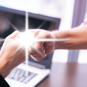 Two people fist-bumping in front of a laptop, with a glowing spark symbolizing trust and connection.