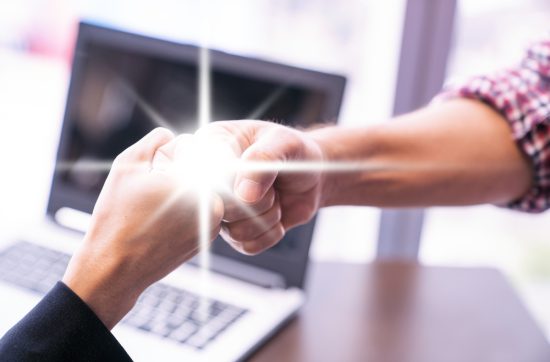 Two people fist-bumping in front of a laptop, with a glowing spark symbolizing trust and connection.